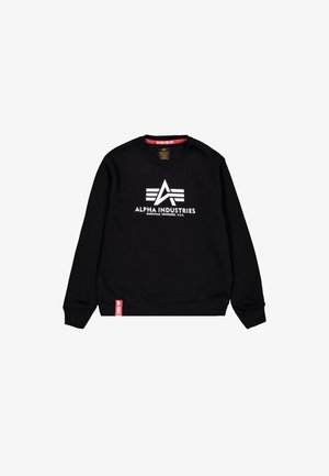 Sort crewneck sweatshirt med hvid Alpha Industries-logo og tekst centreret på forsiden, rød mærkat nær bunden på hvid baggrund.