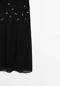 Jupe noire transparente avec motifs floraux brodés et sequins sur la partie supérieure, tissu fluide et ourlet droit.
