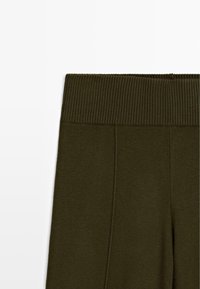 Leggings vert olive avec une ceinture côtelée et une texture lisse, accompagnés de coutures visibles sur les côtés pour plus de détails.