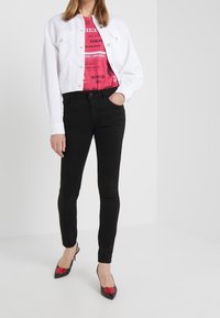 Bílá džínová bunda, růžové tričko s grafikou, černé úzké džíny a černé podpatky s červenými srdíčky. Jednoduchý design s přiléhavým střihem.