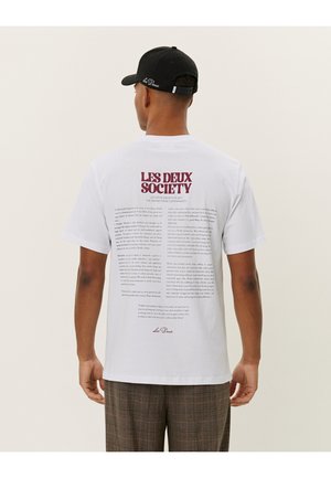 White cotton t-shirt featuring printed text on the back in burgundy. The front is plain. The wearer is also wearing a black cap.