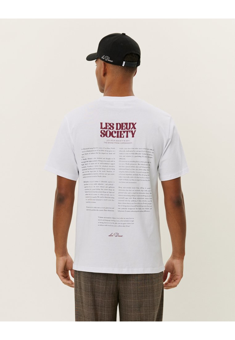 White cotton t-shirt featuring printed text on the back in burgundy. The front is plain. The wearer is also wearing a black cap.