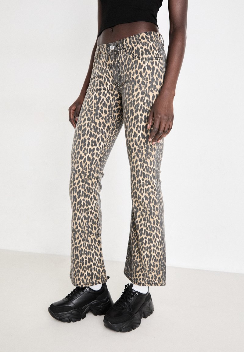 Pantalons évasés imprimés léopard en beige et noir, avec un design à cinq poches, taille cintrée et léger éclat. Associés à des baskets noires.
