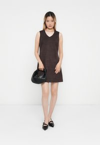 Brown sleeveless dress with a V-neck, made of suede-like material. Paired with a black leather bag and black pointed-toe shoes.