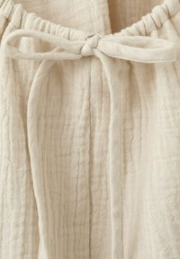 Gros plan d'un tissu beige texturé avec un nœud de cordon serré, montrant les détails d'une surface douce et froissée.