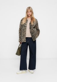 Καρό παλτό με λεοπάρ σχέδιο, κρεμ πουλόβερ πλεκτό, φαρδιές σκούρες τζιν παντελόνες, λευκά αθλητικά παπούτσια, κρατώντας ελιά-πράσινη τσάντα. Απλός, σύγχρονος σχεδιασμός.