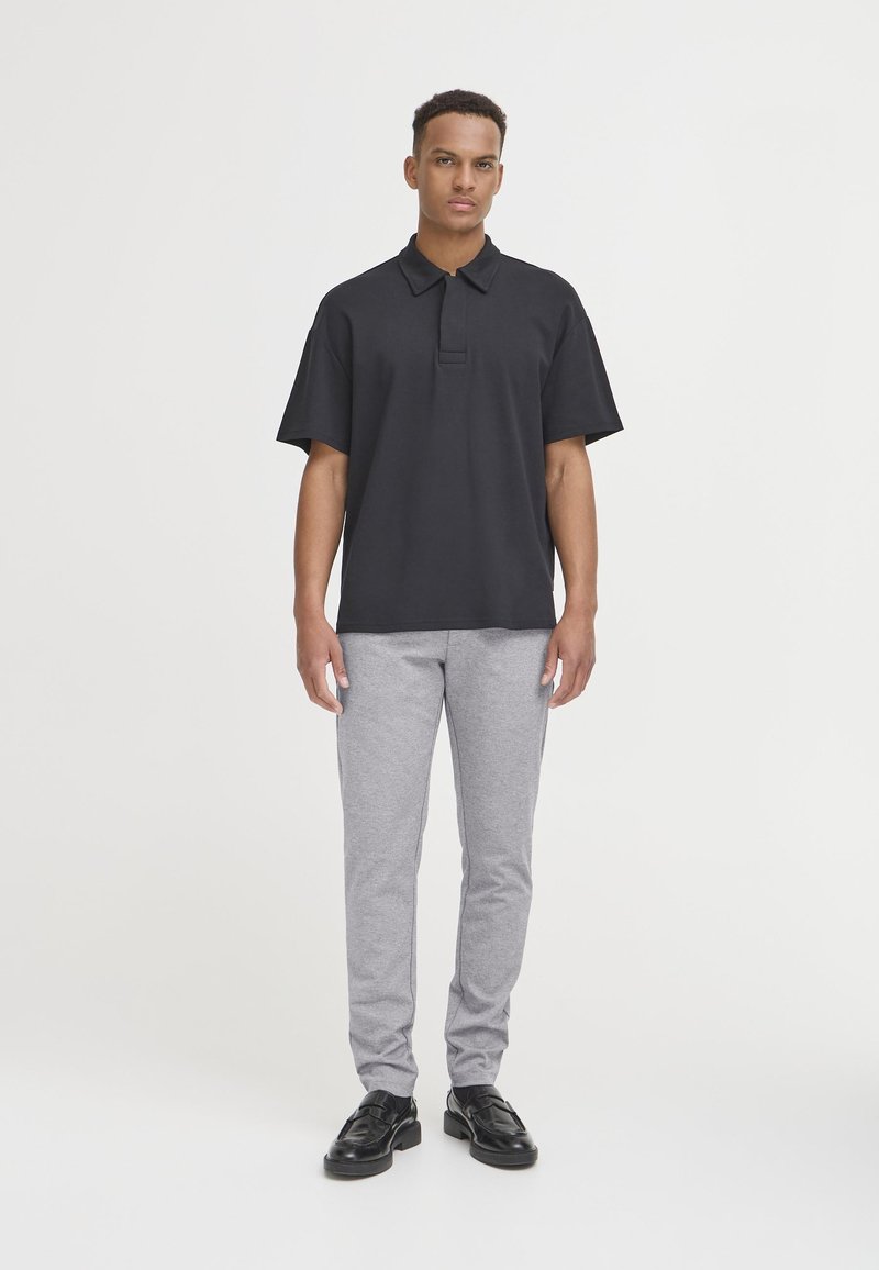 Sort polo skjorte med korte ærmer, flad krave, båret med grå bukser og sorte sko. Simpelt design, behageligt stof og lige pasform.