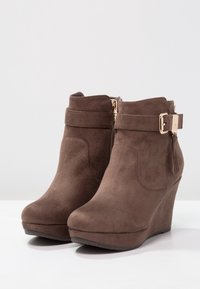 Stivaletti in suede marrone con tacco a rocchetto, dotati di una cerniera laterale e di un'accento decorativo a fibbia sulla cinghia.
