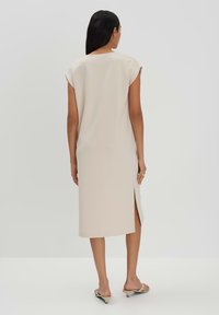 Beiges knielanges Kleid mit kurzen Ärmeln, seitlichem Schlitz, glatter Textur und minimalistischem Design. Getragen mit hellen Slide-Sandalen.