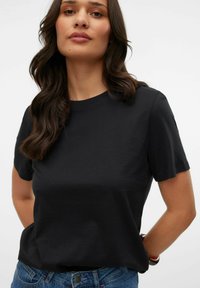 Schwarzes Baumwoll-T-Shirt mit kurzen Ärmeln und rundem Ausschnitt, kombiniert mit blauen Denim-Jeans. Glatte Textur, lässige Passform und minimales Design.