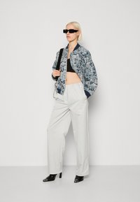 Veste bomber fleurie en bleu marine et blanc, crop top noir, pantalon blanc ample et escarpins noirs pointus. Les accessoires comprennent des lunettes de soleil noires.