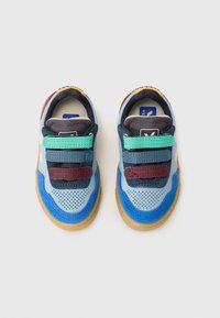 Baskets colorées avec une tige synthétique bleu clair, des superpositions en tissu multicolores, trois bandes velcro et une semelle en caoutchouc marron.