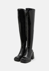 Bottes noires brillantes montant jusqu'au genou, avec un talon épais, un bout arrondi et une fermeture éclair latérale. Texture lisse et design élégant.