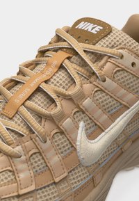 Ταμπά αθλητικό παπούτσι Nike με λεπτομέρειες από δίχτυ και δέρμα, άσπρο κεντημένο λογότυπο swoosh, μπεζ κορδόνια και ετικέτα «MJ Bowman Series» στη γλώσσα.