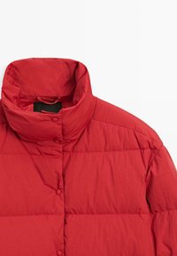Veste matelassée rouge à col montant avec fermetures par boutons-pression, montrant les détails du haut de l'avant et des épaules sur fond blanc.