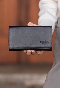 Black leather wallet with a smooth texture, rectangular shape, and embossed logo. Features stitched edges and a fold-over design.