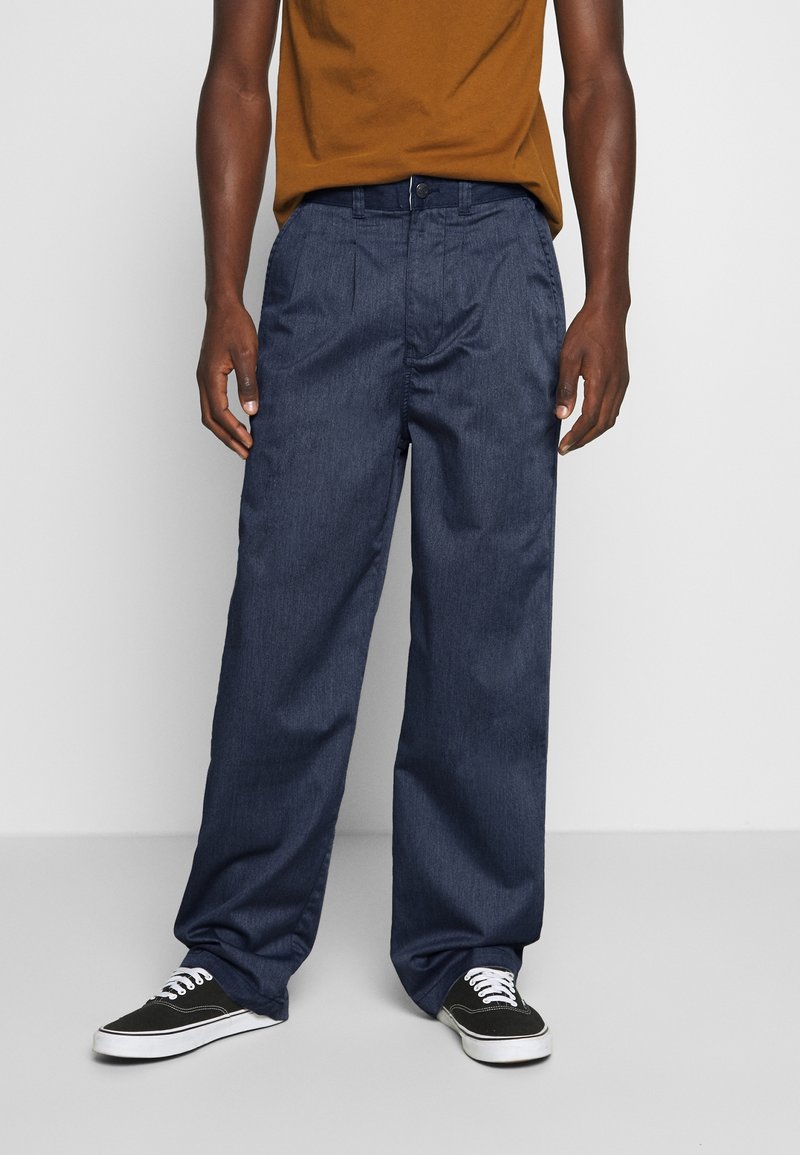 Mörkblå denimbyxor med rak passform, med knappstängning och framfickor, i kombination med svarta kanvas sneakers.