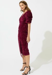 Robe en sequins bordeaux avec de courtes manches bouffantes, design enveloppant et ourlet mi-long. Associée à des talons noirs à brides.