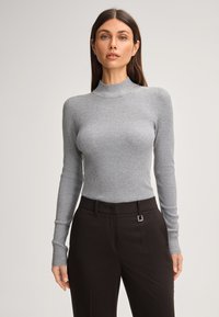 Grijze geribbelde turtleneck trui met lange mouwen, gecombineerd met zwarte, op maat gemaakte broek met een metalen accent op de tailleband.