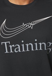 Camiseta de algodón negra con un gráfico blanco de un swoosh estilizado de Nike y la palabra "Training" en gris, con una textura suave.