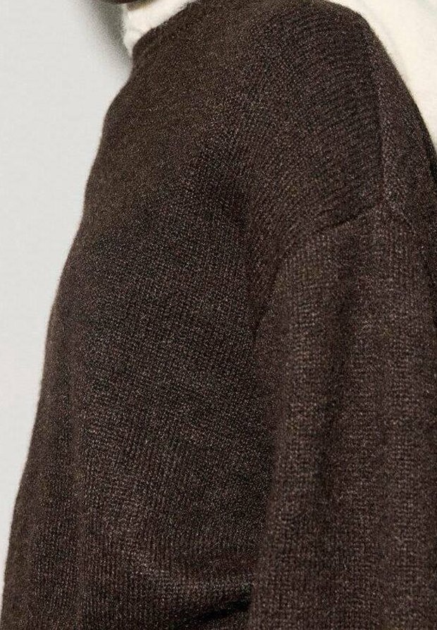 Gros plan d'une personne portant un pull en maille marron foncé avec un motif texturé et un col montant.