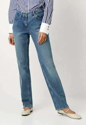 Hellblaue Jeans aus Denim mit geradem Schnitt, Fünf-Taschen-Design und leicht ausgefransten Säumen. Getragen mit einem gestreiften Hemd und beigen Schuhen.