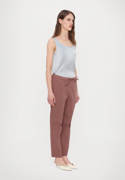 Jasnoniebieska satynowa bluzka na ramiączkach z okrągłym dekoltem, w połączeniu z różowymi spodniami z elastycznym pasem. Modelka nosi białe klapki na obcasie.