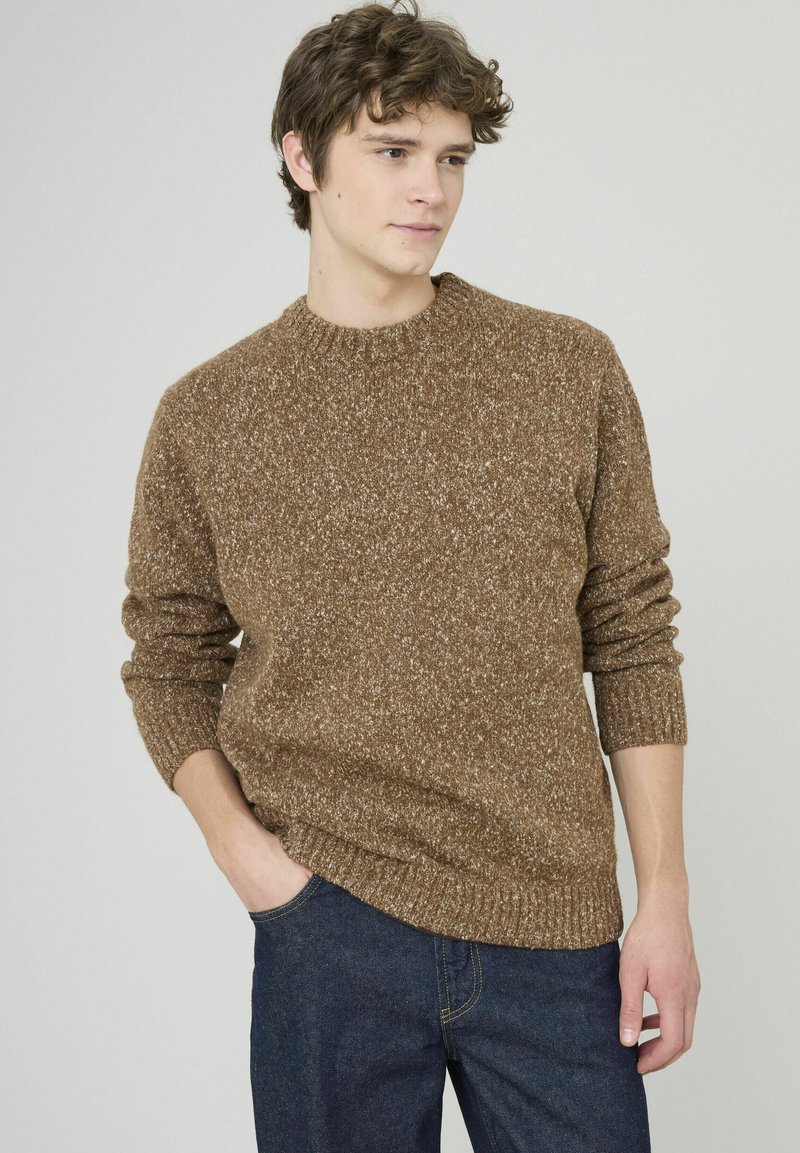 Pull en maille brun avec un col rond, des poignets et un ourlet côtelés, accompagné d'un jean en denim foncé. Le tissu présente un motif moucheté.