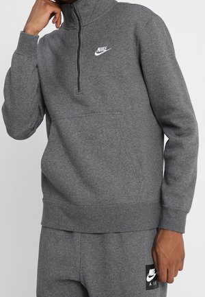 Osoba nosząca szarą bluzę Nike z zamkiem na ćwierć długości oraz pasujące szare spodnie dresowe Nike Air z widocznymi logo na obu.