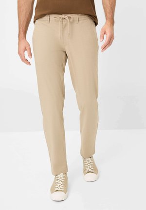Beige, lightweight pants with an elastic waistband and drawstring. Straight-leg design with side pockets. Paired with beige sneakers.