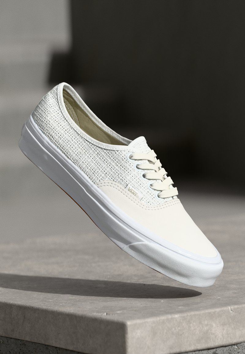 Witte canvas sneakers met een gestructureerde bovenkant, witte veters en een rubberen zool. Heeft een minimalistisch ontwerp met subtiele branding aan de zijkant.