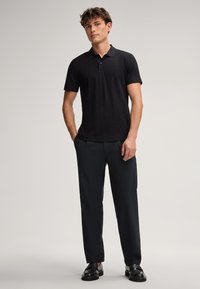 Schwarzes kurzärmliges Poloshirt mit strukturiertem Rautenmuster, kombiniert mit dunklen Hosen und schwarzen Dressschuhen.