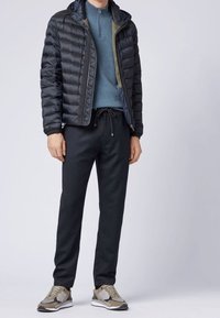 Puchowa czarna kurtka, niebieski sweter, czarne dresy oraz szaro-brązowe trampki z teksturowanymi akcentami. Kurtka ma kaptur i zamek błyskawiczny.