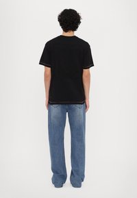 Svart t-skjorte med korte ermer og en teksturert design på baksiden, parret med løstsittende blå denimjeans.
