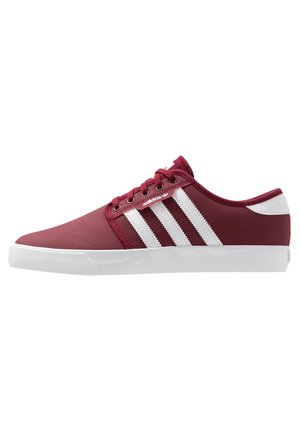 Baskets basses Adidas bordeaux avec semelle en caoutchouc blanche et trois bandes blanches sur le côté, dotées de lacets et du logo de la marque.