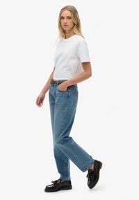 Jeans de mezclilla azul con un corte recto, combinados con una camiseta de algodón blanca ajustada. Zapatos de cuero negro con detalle de borlas.