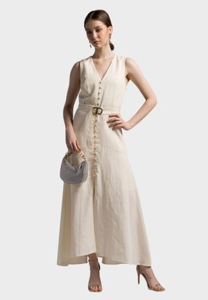 Largo vestido beige claro con escote en v, frente con botones y un cinturón en la cintura. Combinado con un pequeño bolso plateado y sandalias de tiras.