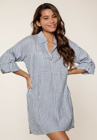 Vestido camisero de rayas en azul marino y blanco, con cuello clásico, bolsillos con botones y mangas arremangadas. Tejido de algodón suave, de longitud a la rodilla.