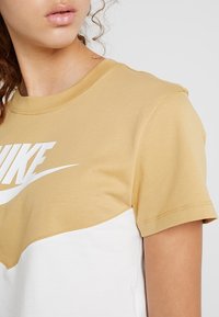 Cotton t-shirt med en guld överdel och vit underdel, med en stor vit Nike-logotyp framtill, rund hals och korta ärmar.