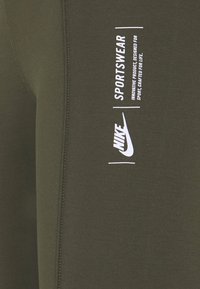 Ciemnooliwkowe spodnie sportowe z białym logo i napisem "Nike". Charakteryzują się miękkim materiałem, elastycznym pasem i pikowanymi detalami.