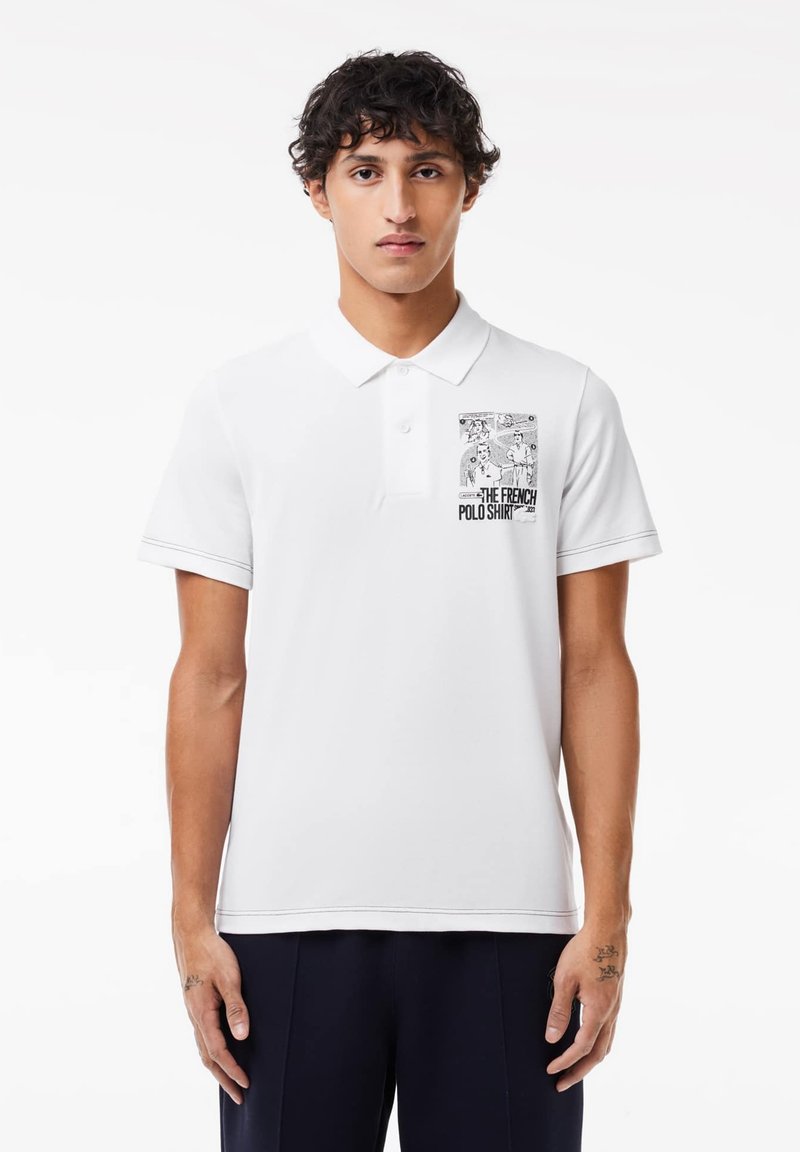 Polo blanc avec une petite impression graphique noire sur la poitrine gauche. Manches courtes avec des coutures contrastées et un design de col classique.