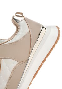 Beige sneaker with quilted synthetic leather, metallic accents, and a white cushioned sole. Features a textured upper and a pull tab.