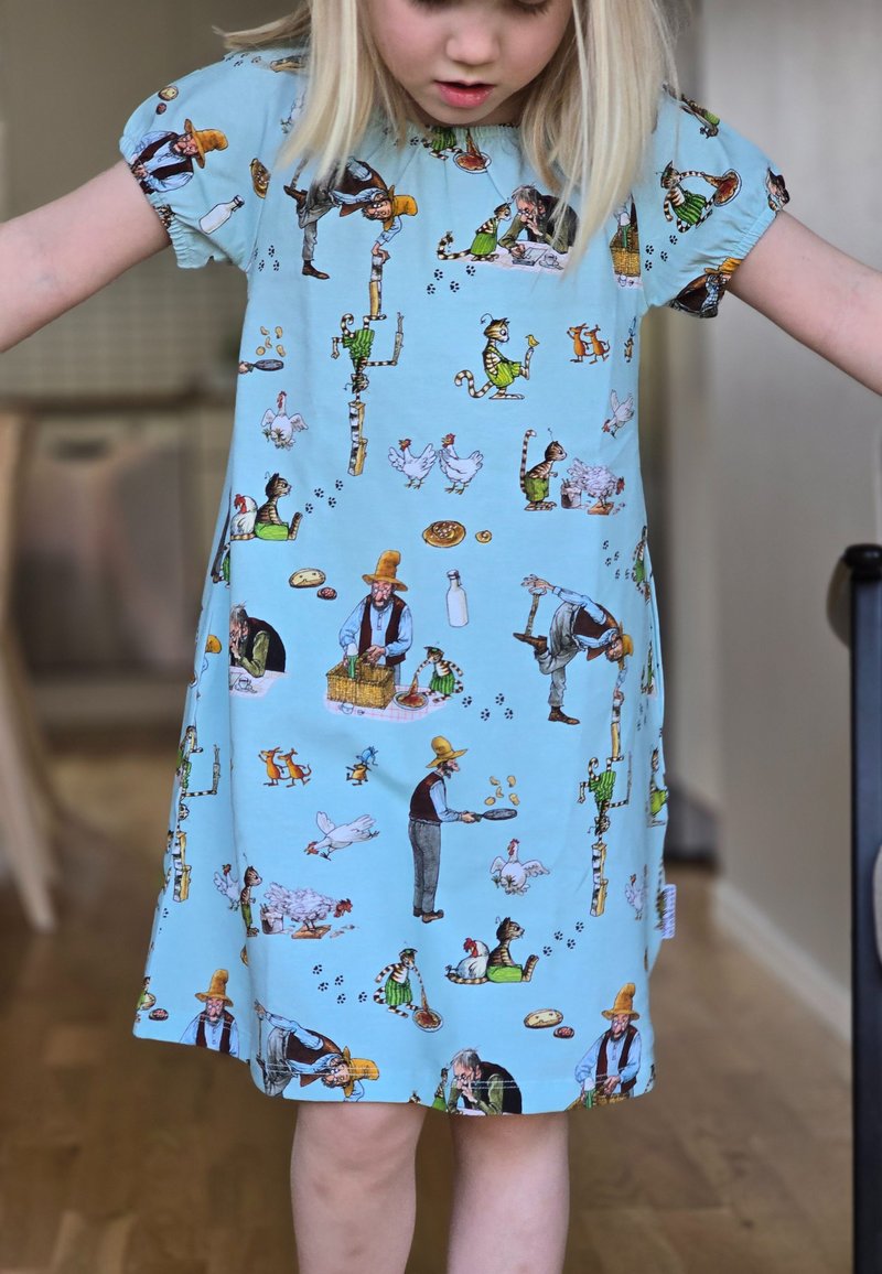Sininen mekko, jossa on erilaisia viehättäviä kuvastoja hahmoista ja eläimistä, lyhyet hihat ja löysä, mukava istuvuus.