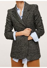 Grå tweedblazer med struktureret design, hakkraver, to forlommer og let polstrede skuldre, lagdelt over en lyseblå skjorte.