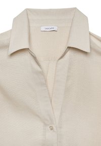 Camicia di lino beige con colletto a punta, caratterizzata da una profonda scollatura a V e chiusura con un bottone. Texture liscia; etichetta con la scritta "Lascana."