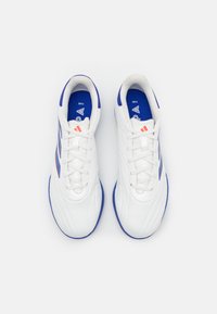 Zapatillas deportivas blancas con parte superior sintética lisa, acentos azules y detalles rojos. Cuentan con cierre de cordones y suela texturizada.