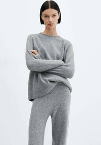 Pullover grigio lavorato a maglia con scollatura rotonda e polsini a coste, abbinato a pantaloni grigi lavorati a maglia coordinati. Tessuto morbido e strutturato.