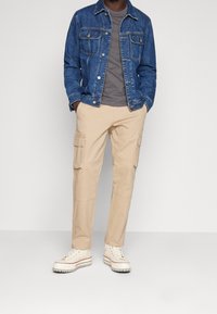 Denimjacka, grå t-shirt, beige cargobyxor och vita sneakers med röda accenter. Har fickor och en avslappnad passform.