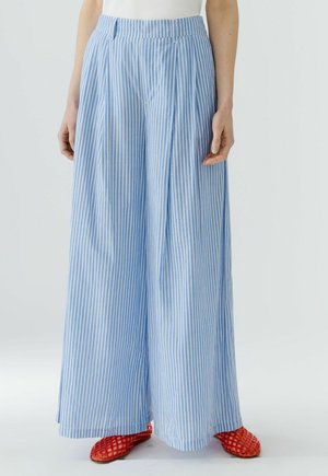 Pantalon large à rayures verticales bleues et blanches porté avec des chaussures plates tissées rouges sur une personne debout.