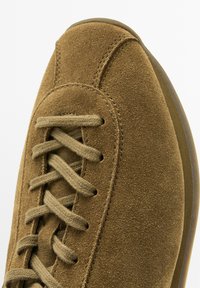 Brune ruskind sneakers med rund tå, flade snørebånd og syninger; gummisål med let skridsikkerhed. Glat tekstur hele vejen igennem.